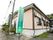 歩道との境に施設名が書かれた緑色の縦型の看板が設置されている。建物の前にはさまざまな高さの樹木が植えられている。