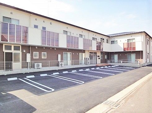 広い駐車場があり、たくさんの窓が付いた建物。ブラウンと白の２階建ての建物はベランダも付き、明るい雰囲気。
