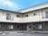 エル字型の建物は２階建てで広い駐車場やベランダがあり、青い空が広がっている。