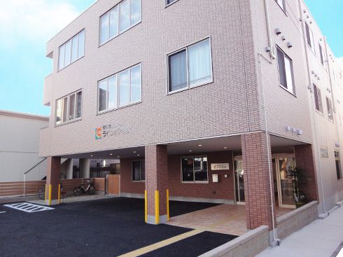 駐車場がある３階建ての建物の外壁はブラウンのレンガ調。出入り口周辺まで点字ブロックが敷かれ、玄関は自動ドア。