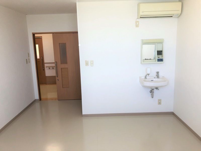 家具や家電は置かれていない部屋の右側には車いす対応の洗面所とエアコンがあり、左側にはドアがある。