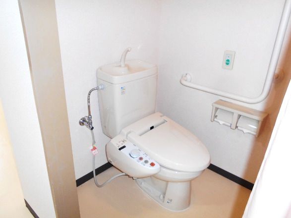エル字型の手すりや呼び出しボタン、トイレットペーパーホルダーが設置されたトイレ。