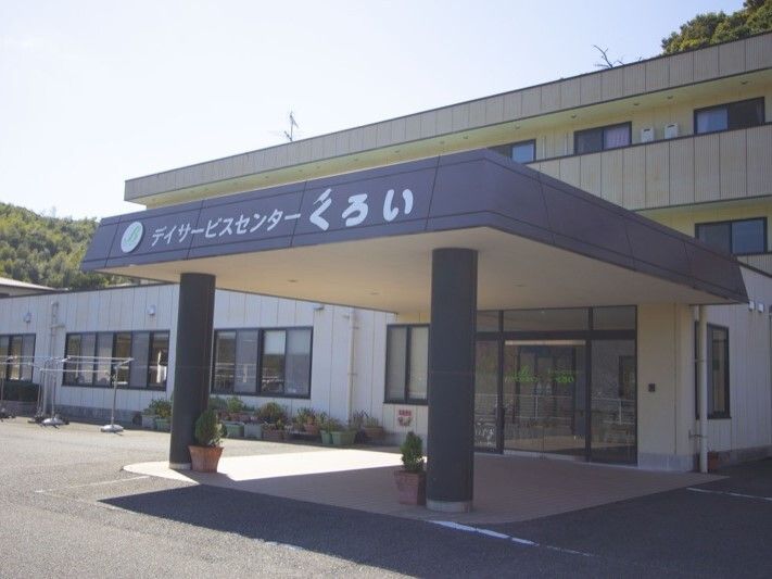 大きくデイサービスの名前が書かれた車寄せが付いた2階建ての建物。日当たりのいい場所に建っている。