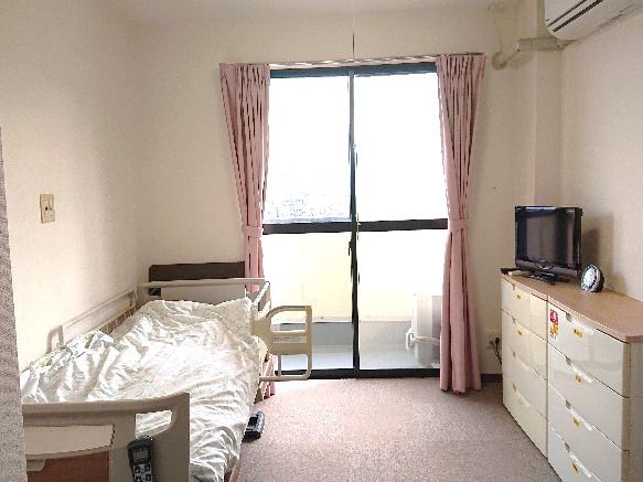 寝具付きのベッドが置かれた部屋にはタンスやテレビもあり、カーテンが付いた窓もある。