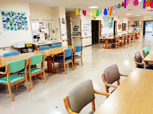 ブルーやグリーン、茶色の椅子がセットされたダイニングテーブルセットが複数置かれたスペース。