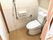 オレンジの呼び出しボタンが付いたトイレにはエル字型の手すりがあり、カーテンで開け閉めするタイプ。