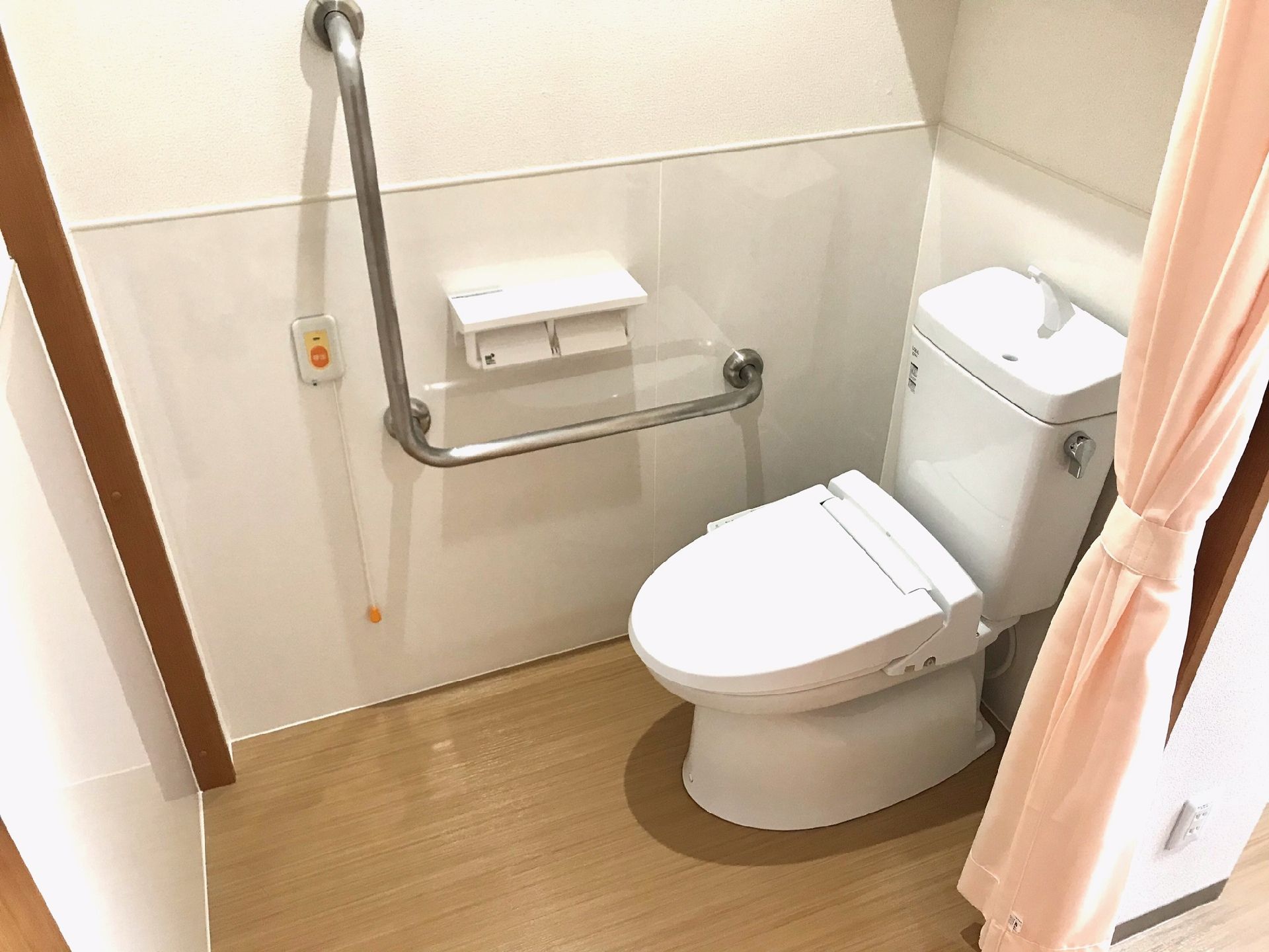カーテンで開け閉めするタイプのトイレが設置されている。呼び出しボタンや手すりがある。