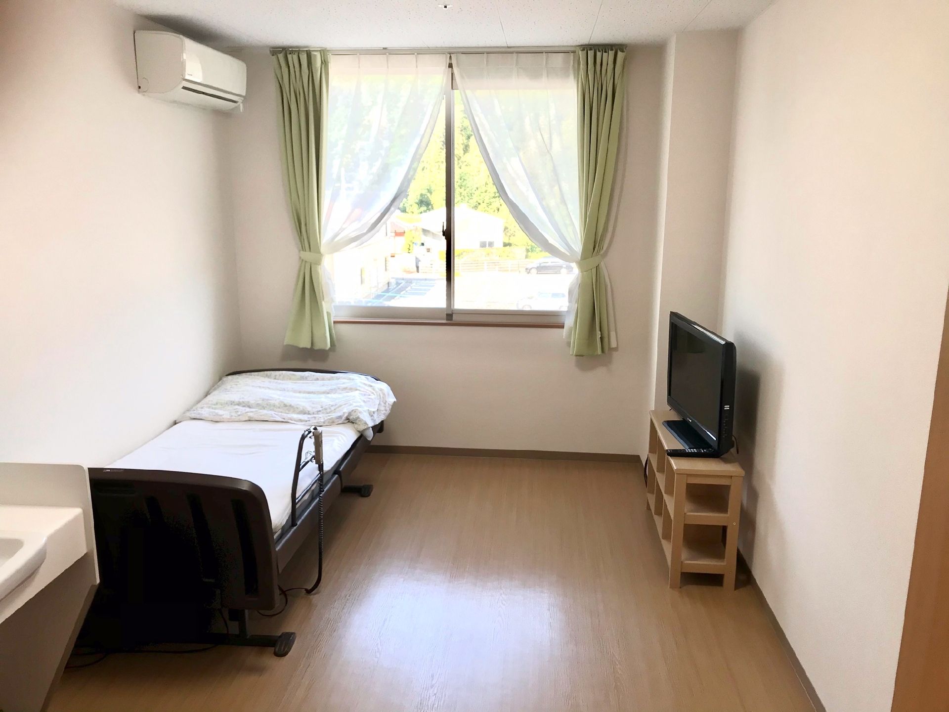 エアコン付きのフローリングの部屋には寝具付きのベッドやテレビ、車いす対応の洗面所がある。