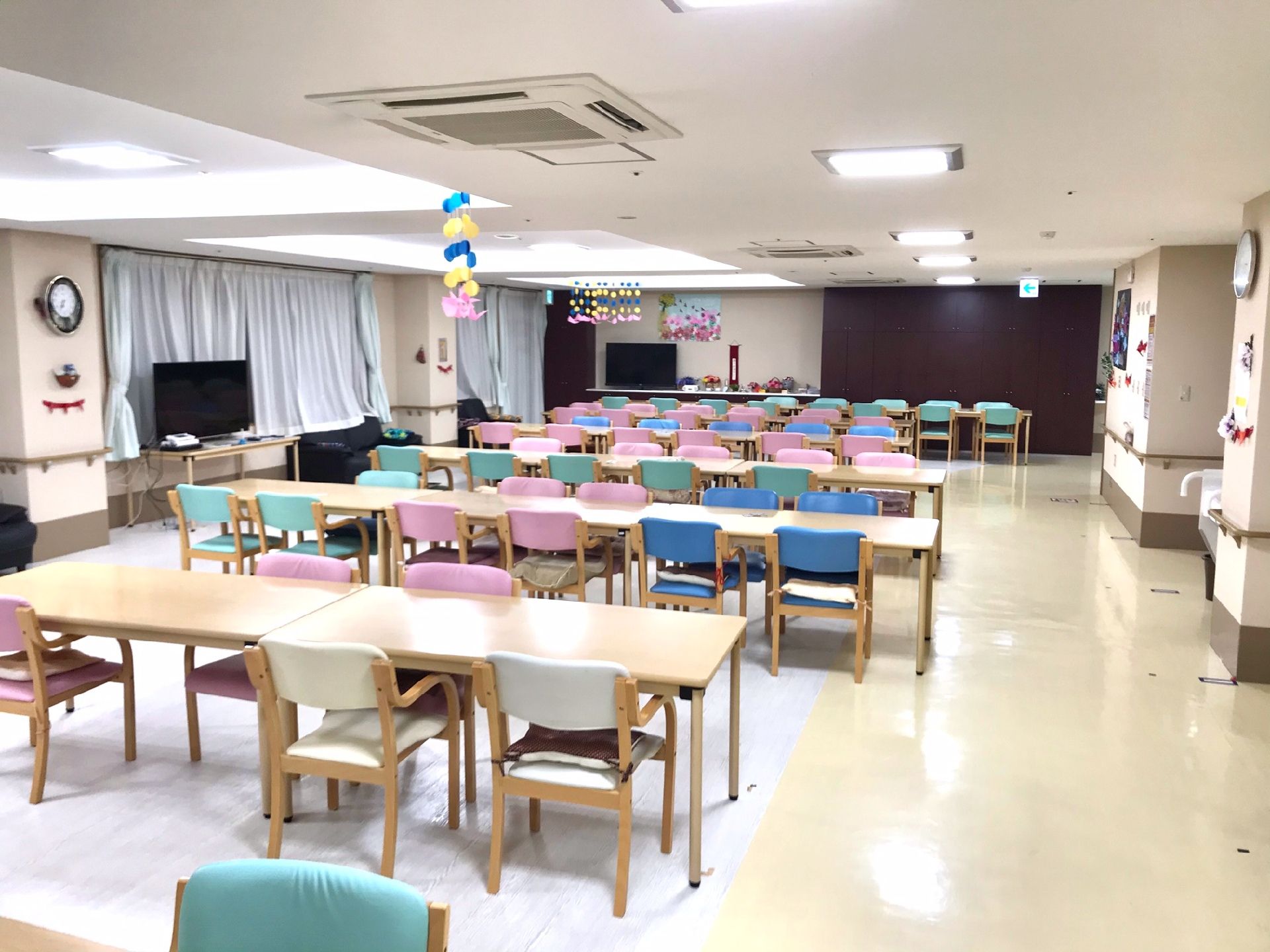 カラフルな椅子がセットされたダイニングテーブルセットが複数置かれているスペースにはテレビもある。