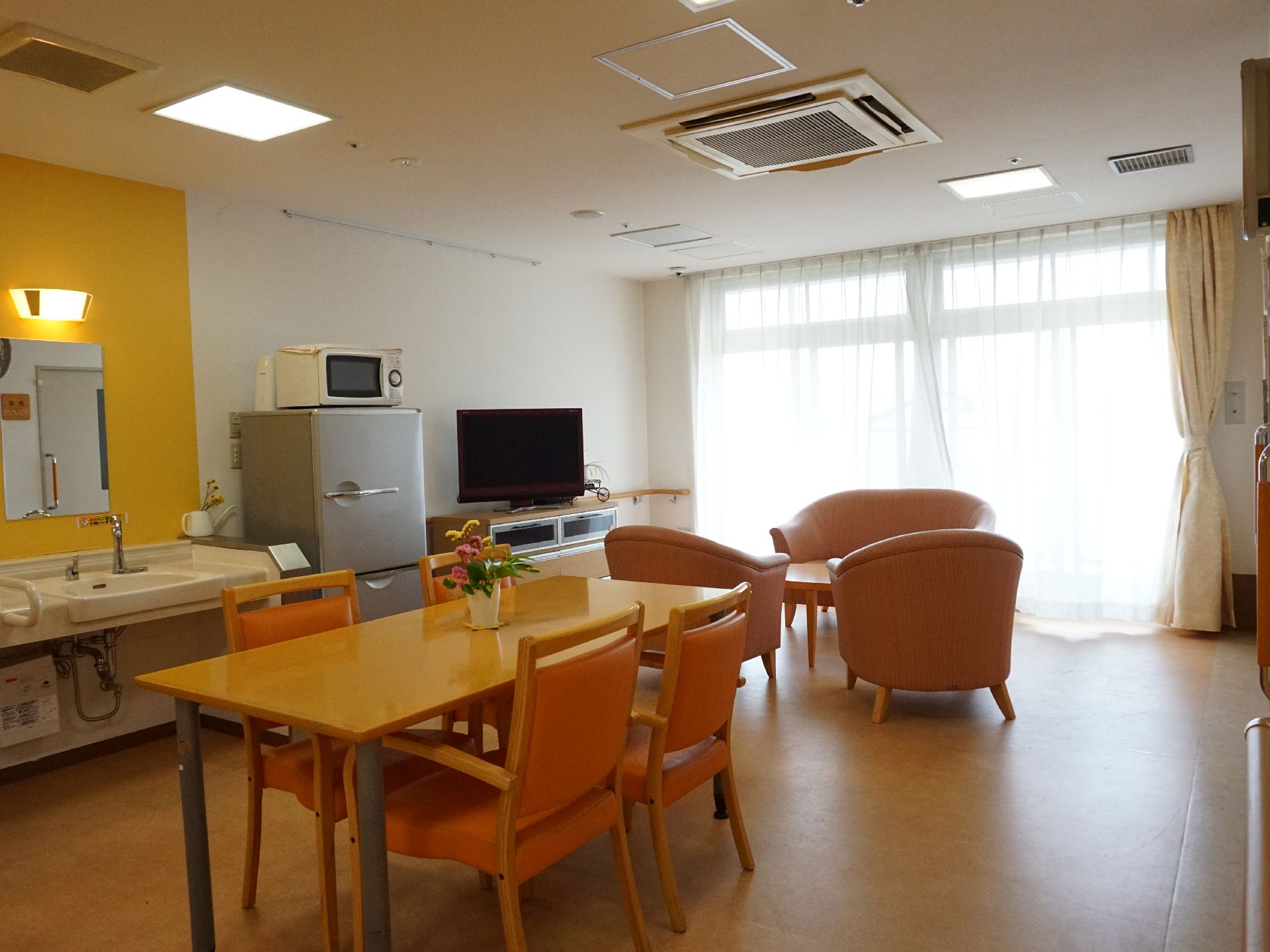 テレビ、テーブル、椅子が設置され、窓から陽光が入っているリビング