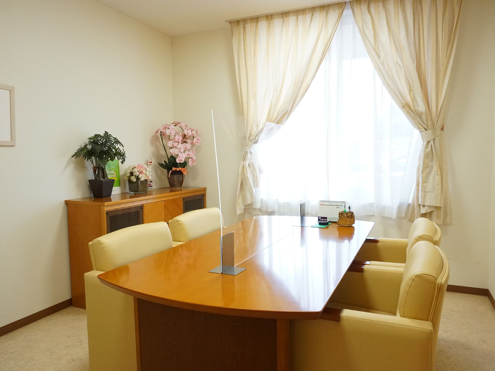 テーブルを挟んで椅子が置かれ、棚に花が飾られている部屋