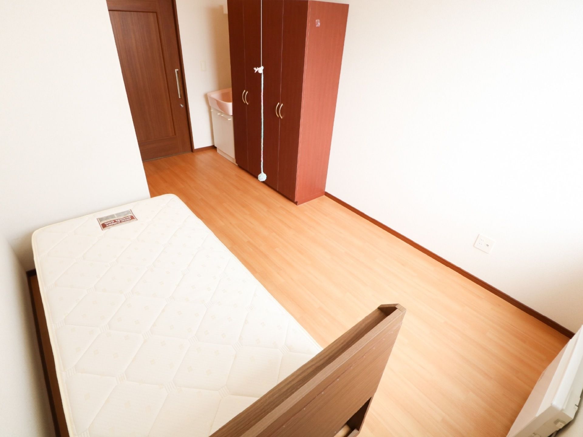 白と木目を基調とした居室である。洗面台、収納庫を備え、壁際にベッドを配置している。壁際にヒーターを設置している。