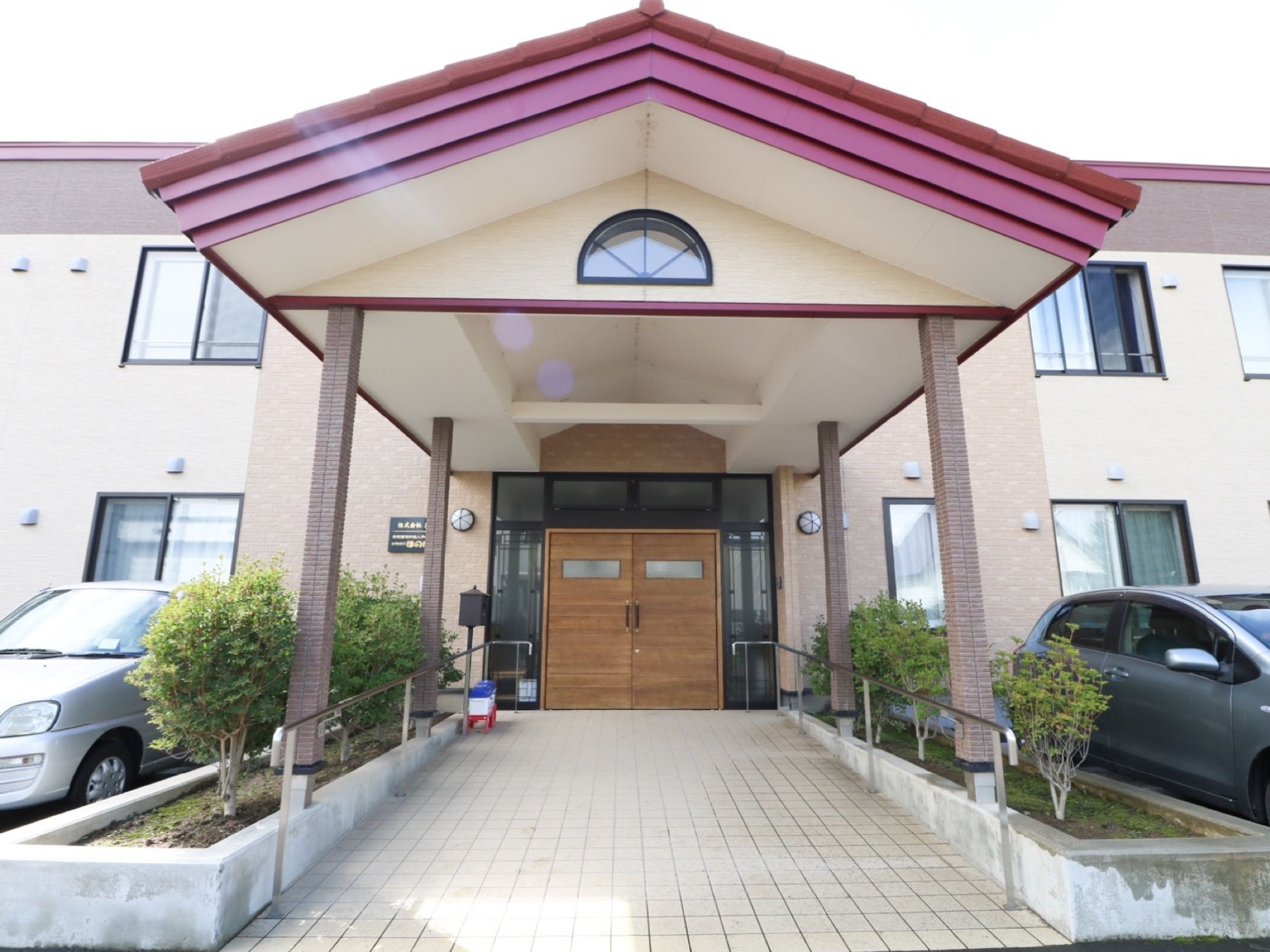 2階建ての建物である。外壁は淡いベージュ調に施されている。玄関付近には駐車場が備わっており、車が2台停められている。