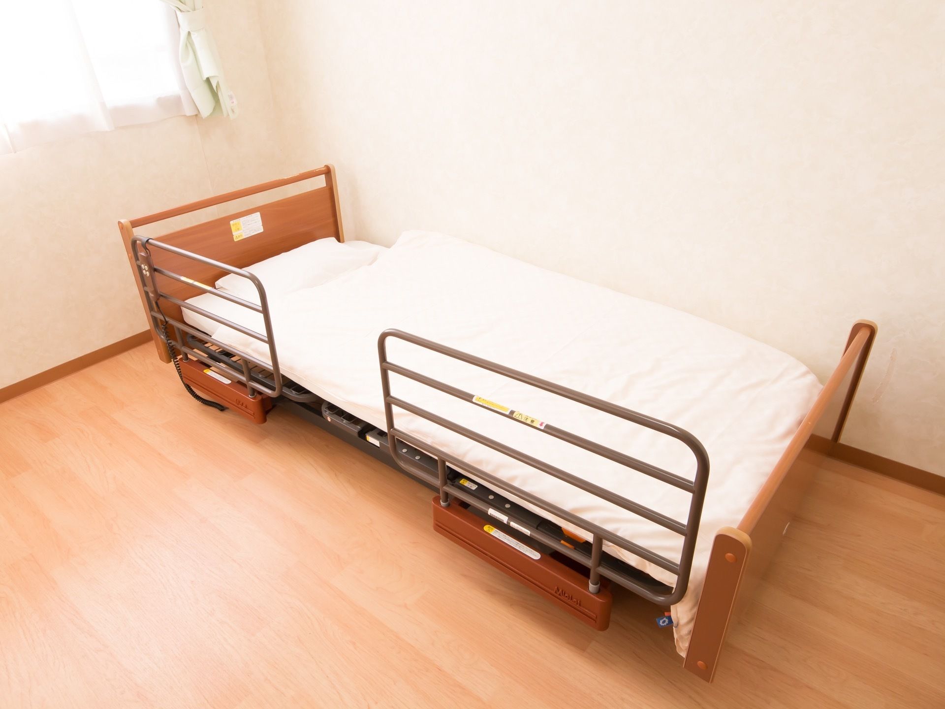 真っ白な壁にフローリングの居室で、壁に沿ってベッドが置いてある。窓から日光が良く差し込んでおり、レースカーテンがついている。