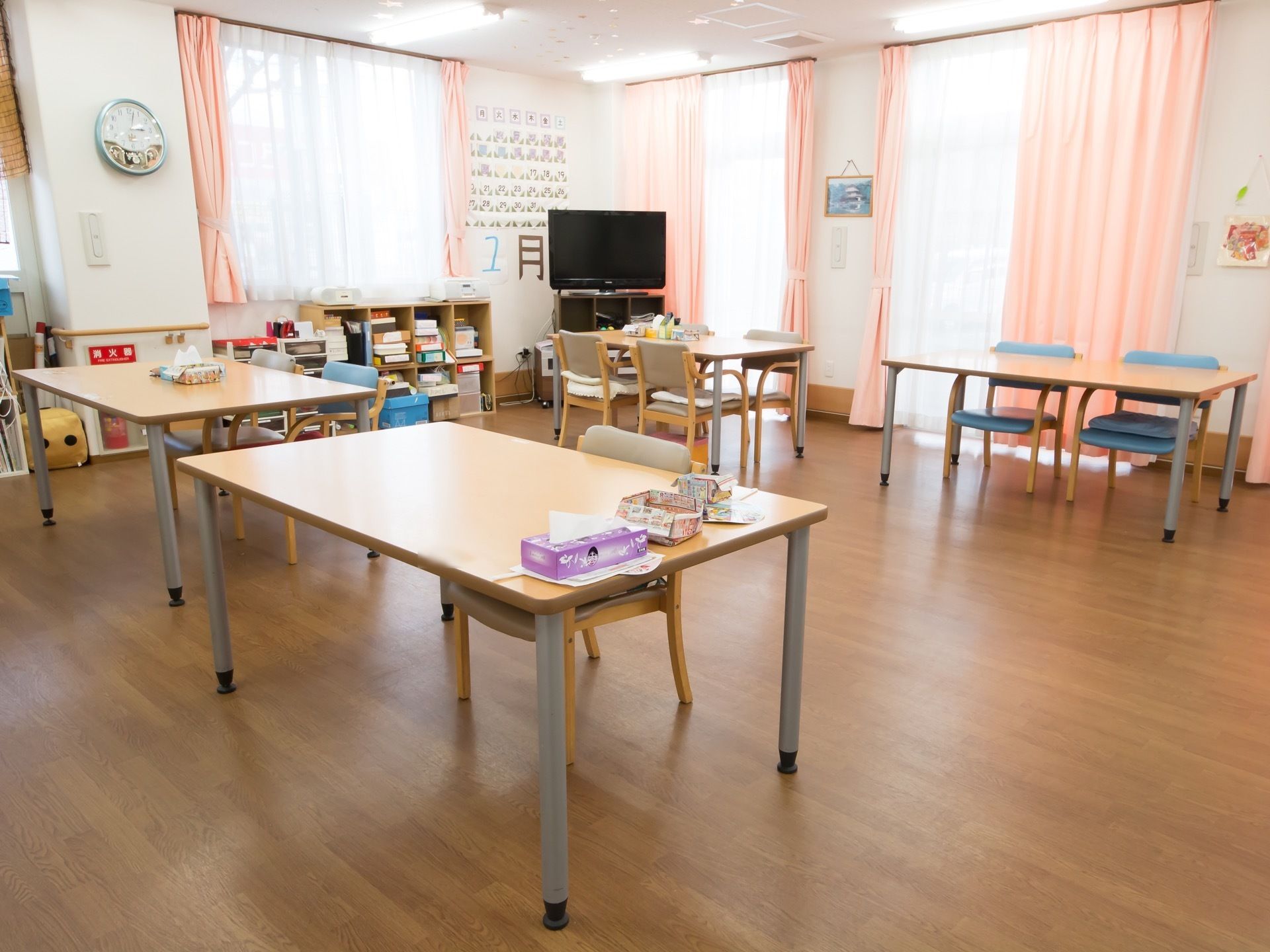 部屋の隅にはテレビが置いてあり、その左側にはその月が大きな文字で書かれている。壁に沿って棚があり、箱がたくさん収納されている。