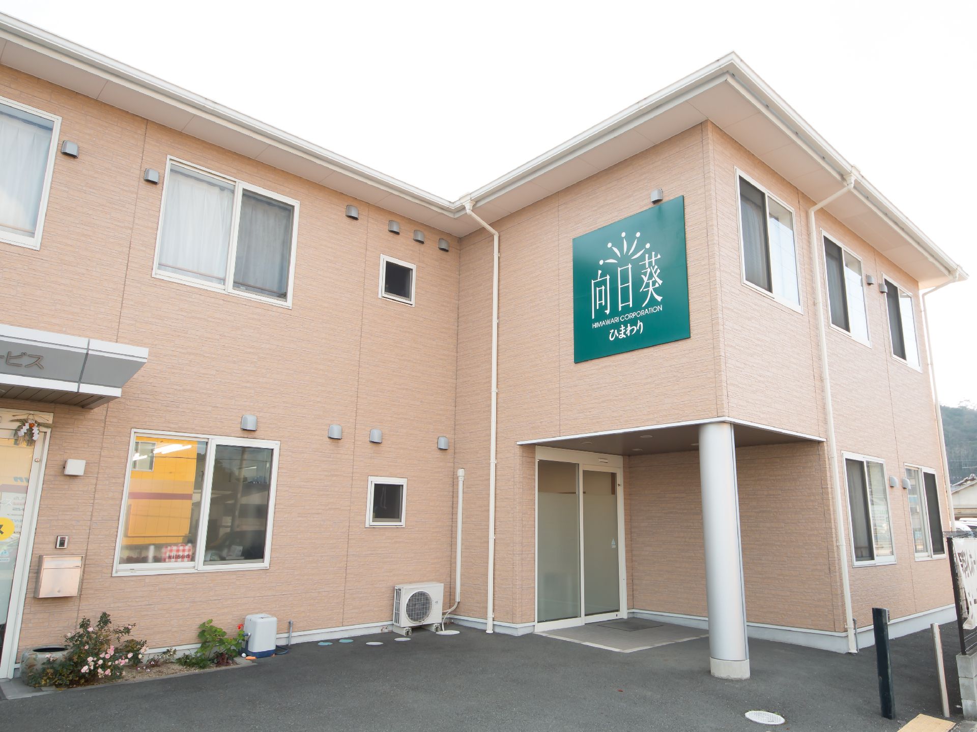 2階建ての建物はブラウン系で統一されていて、玄関前には屋根があり、車が止められている。