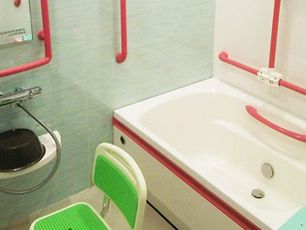 赤い手すりがたくさん付いた浴室には一人用の浴槽が設置され、シャワーチェアやシャワー、洗面器がある。