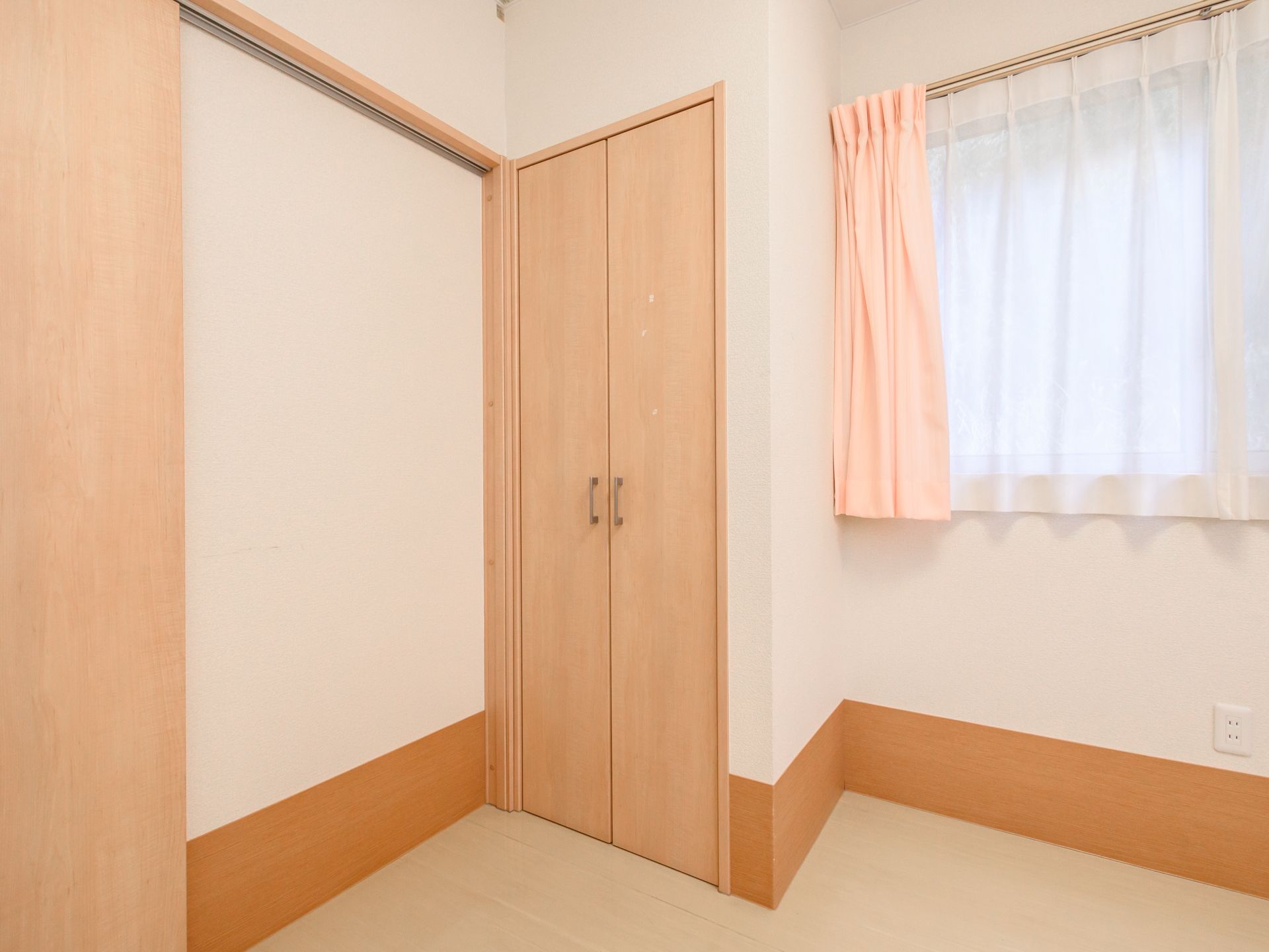 車いすの高齢女性とピンクのエプロンを付けた若い女性スタッフが寄り添い、笑顔で過ごしている。
