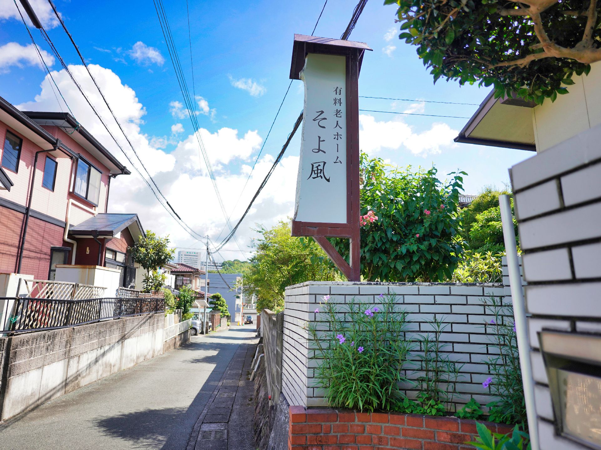 アスファルトの道路沿いにある白いレンガ調の壁に置かれた縦長の看板