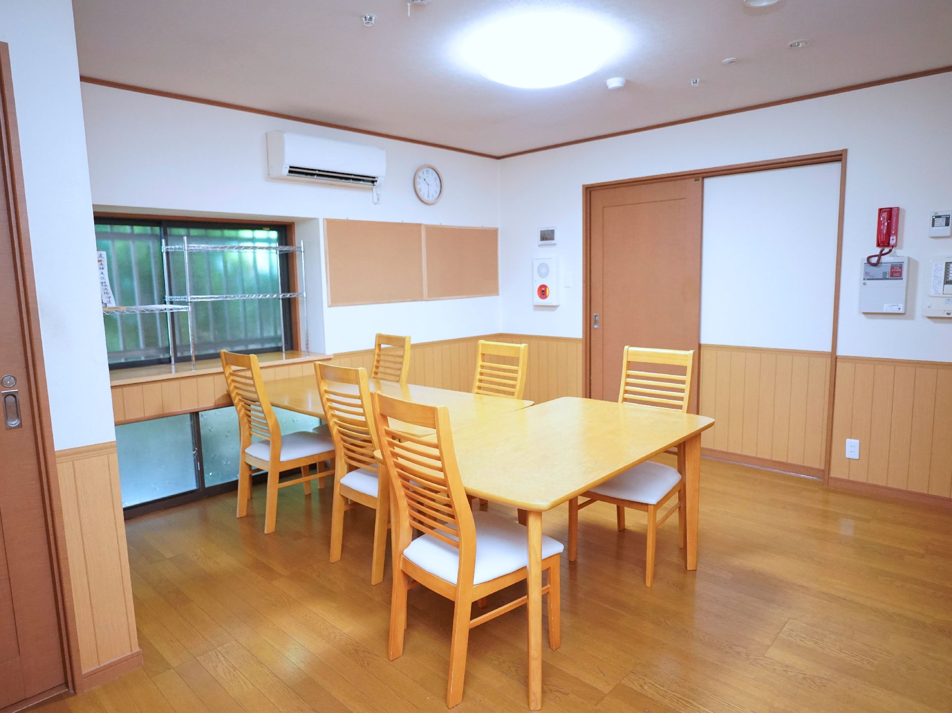木製の机と椅子が置かれた白い壁の広間