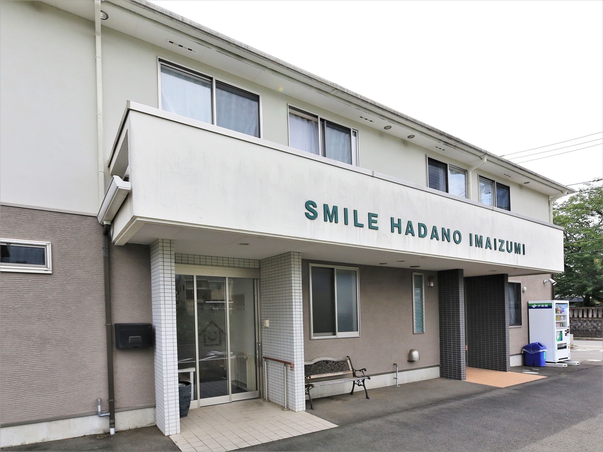 ブラウンを基調とした落ち着いた色合いの建物である。玄関付近には、ベンチや自動販売機が設置されている。