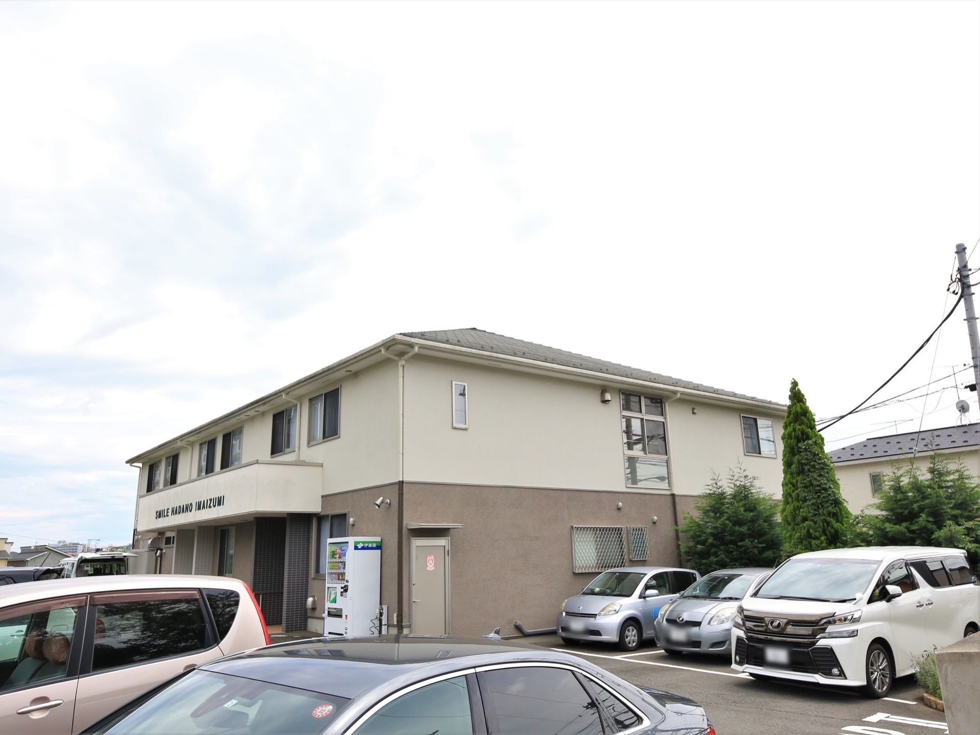 ２階建てのグループホーム。施設敷地内にはアスファルトで舗装された駐車場が完備されており、たくさんの車が停められている。