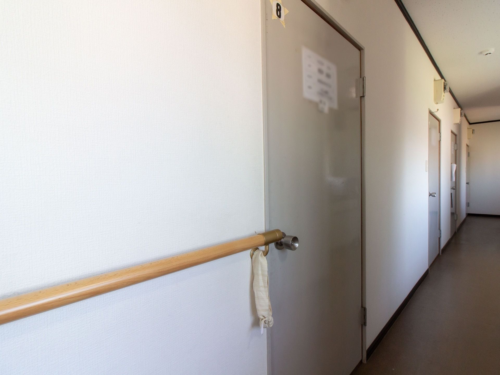 廊下にはグレー色の居室の扉が並んでいる。壁には長い手すりが設置されており、体を支えながら移動することができる。