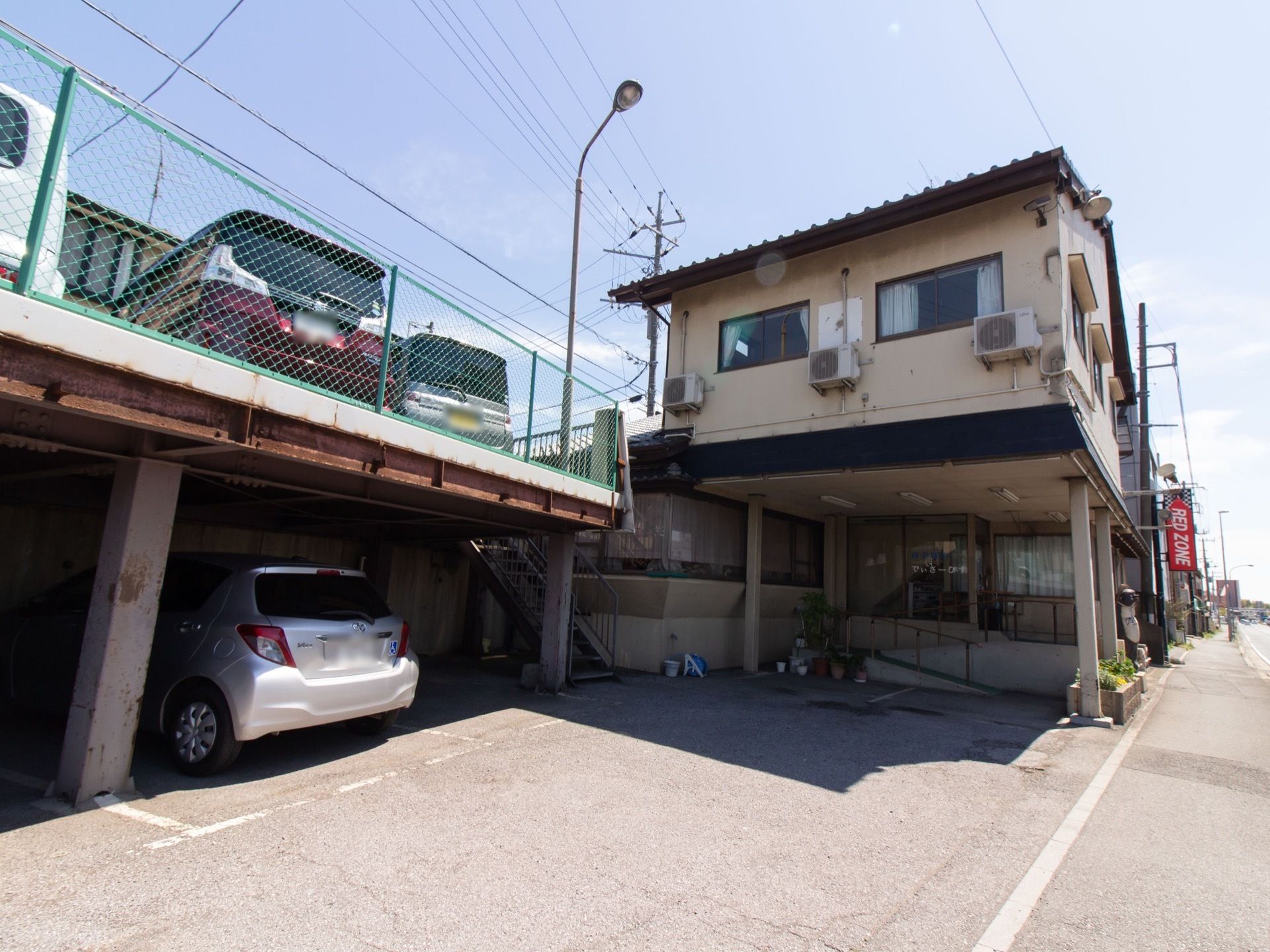 建物のすぐ側に、屋根のついた駐車場が設置されている。身障者マークをつけた普通自動車が、柱の横に停めてある。