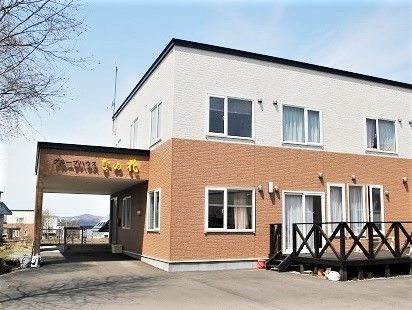 車寄せが付いた玄関。２階建ての建物で外壁の色が２階が白、１階はブラウンとなっている。