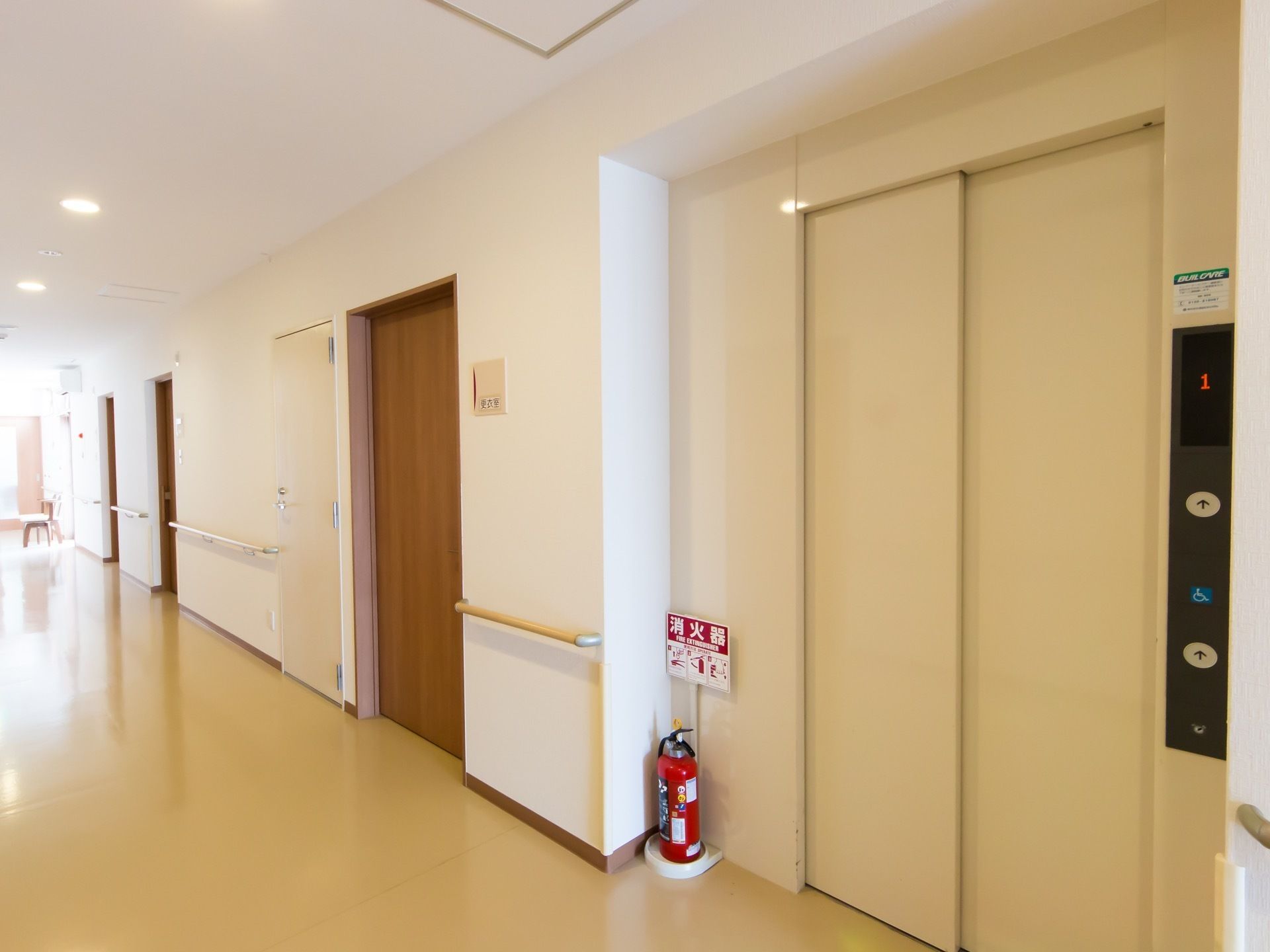 廊下は、突き当たりの扉からの採光で明るくなっている。エレベーター乗降口のすぐ左側に消火器が置かれている。