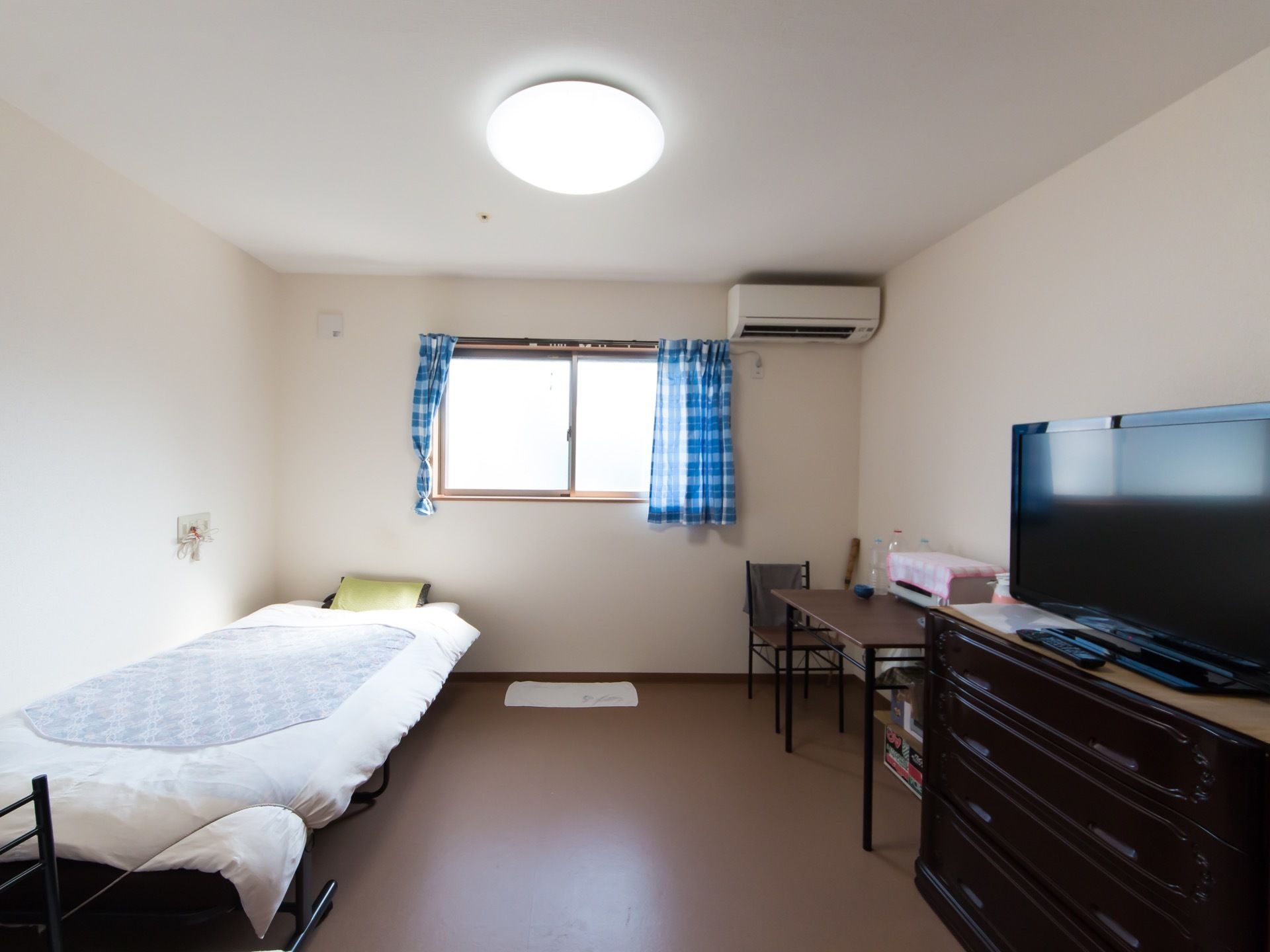 居室にある腰高の窓に、青色のカーテンがかかっている。その右上の壁に、白色のエアコンを設置。