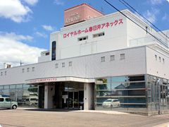 赤い文字でホーム名が書かれた白を基調とし建物は3階建てで、広い敷地内には駐車場があり、車も止められている。