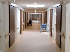 幅の広い廊下の両サイドに車いすが置かれていて、居室のドアはスライド式でドアのすぐそばまで手すりが設置されている。