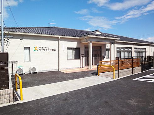 平屋建ての建物で玄関には屋根が付き、外壁にはホーム名が書かれ、敷地内には駐車場もついている。