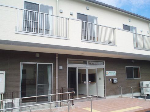 ベランダが付いた2階建ての建物。玄関には手すり付きのスロープがあり、玄関のドアの横にはホーム名が書かれたプレートもある。