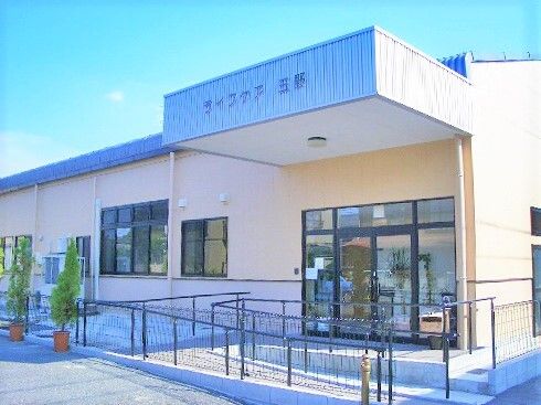 平屋建ての建物で玄関には屋根と手すり付きのスロープが付き、屋根にはホーム名が書かれている。