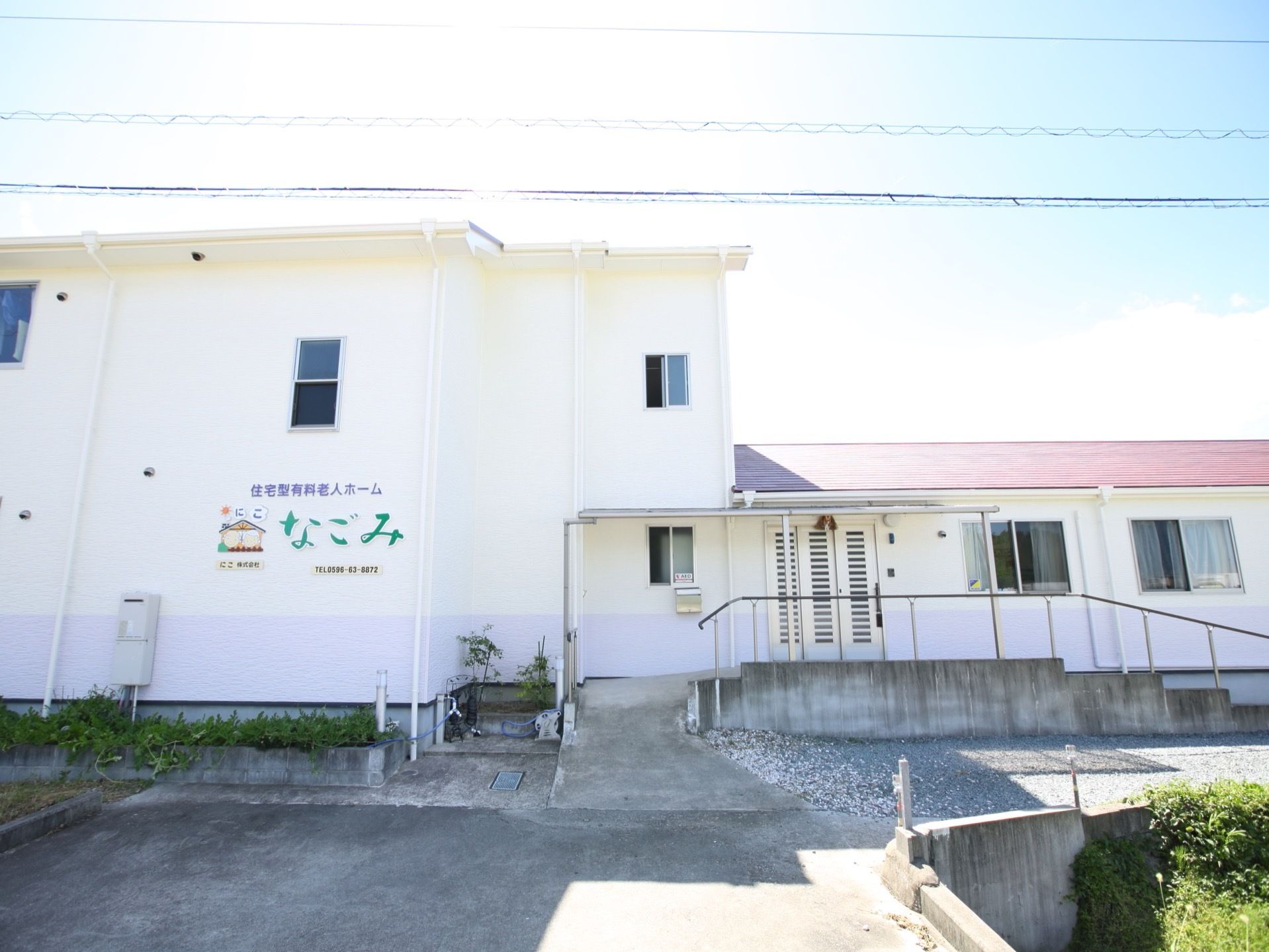 白い２階建てと平家建ての両方を備えた施設である。エントランスまでは手すりの付いたスロープと階段が完備されている。