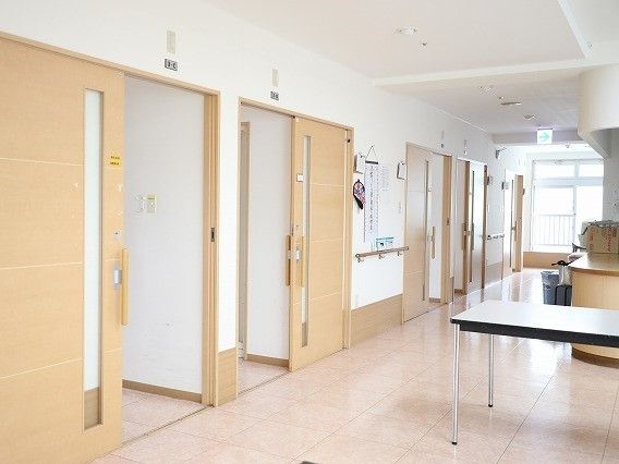 広々とした施設内の廊下とそれに隣接した居室の入り口。手すりがついている廊下