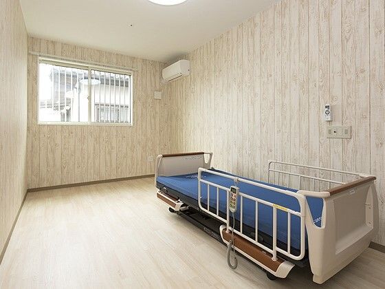 介護ベッドやエアコンが設置されているフローリングの部屋。ベッドサイドには緊急通報装置がある。