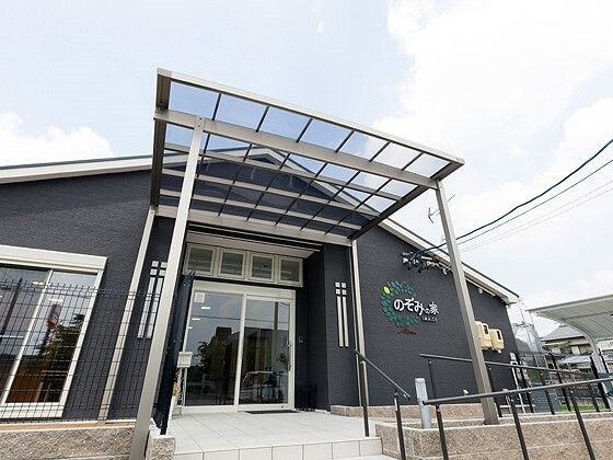 透明の屋根が付いた平屋建ての建物はダークグレーで、玄関先には手すり付きのスロープと階段がある。