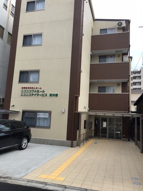 4階建ての建物の前には駐車スペースがあり、車が止められている。玄関までのアプローチには点字ブロックが敷かれている。