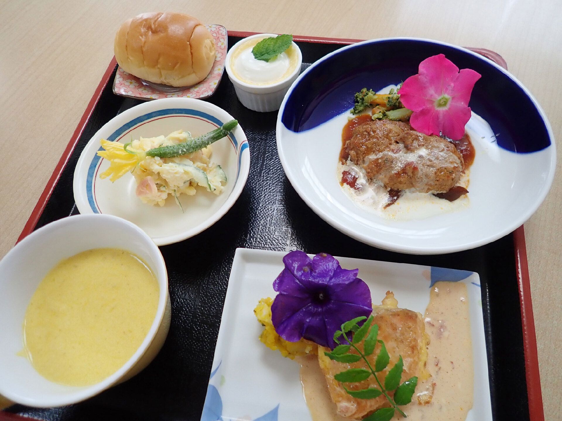 パンやコーンスープが添えられた肉料理がメインの洋風のコース料理。白いデザートもあり、ピンクや紫のエディブルフラワーを飾っている。