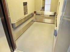大きなエレベーターの庫内にはシルバーの太い手すりが付き、正面には鏡が設置され、サイドには操作パネルが付いている。
