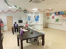 天井や壁に手作りの飾りが飾られたリビング。女性が数名黒いダイニングテーブルについていて、テーブルの上にはティッシュなどが置かれている。