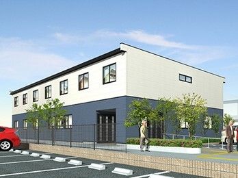 白とダークグレーの2階建ての建物。周辺には木が植えられ、駐車場が設置され、玄関には手すり付きのスロープがあり、明るい雰囲気。
