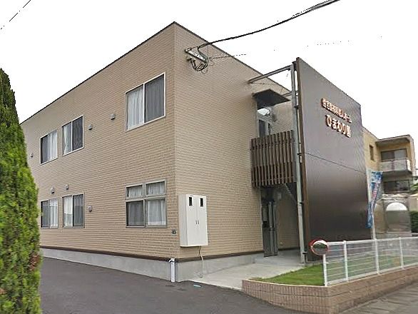 2階建ての建物はブラウンで屋外階段が付き、ホーム名も書かれている。