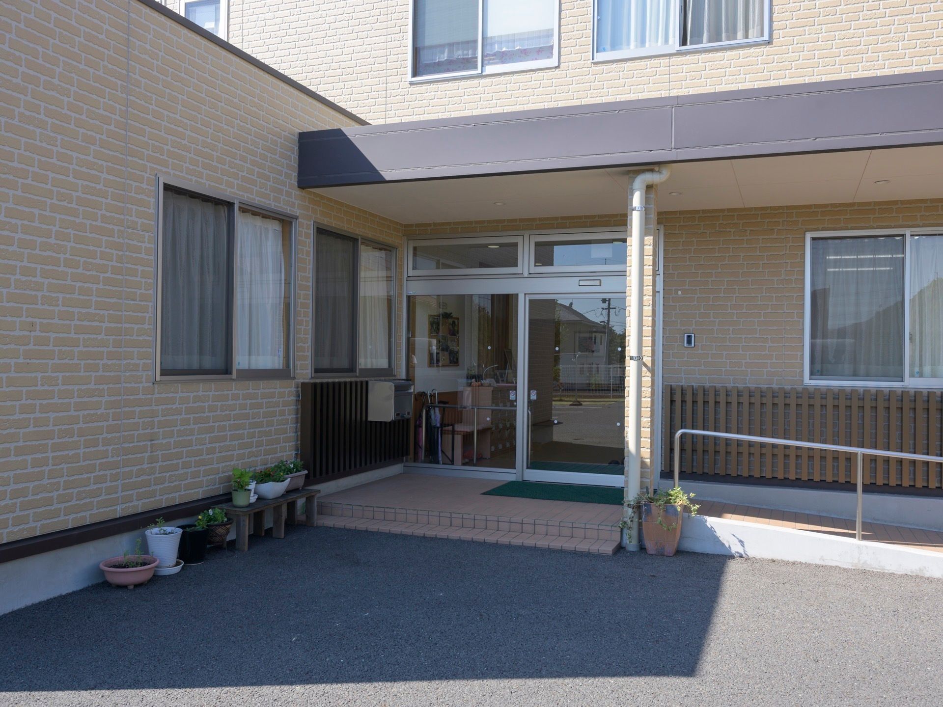 玄関前には、階段と右側に伸びるスロープが設置されている。スロープの方には自立式の手すりが取り付けられている。