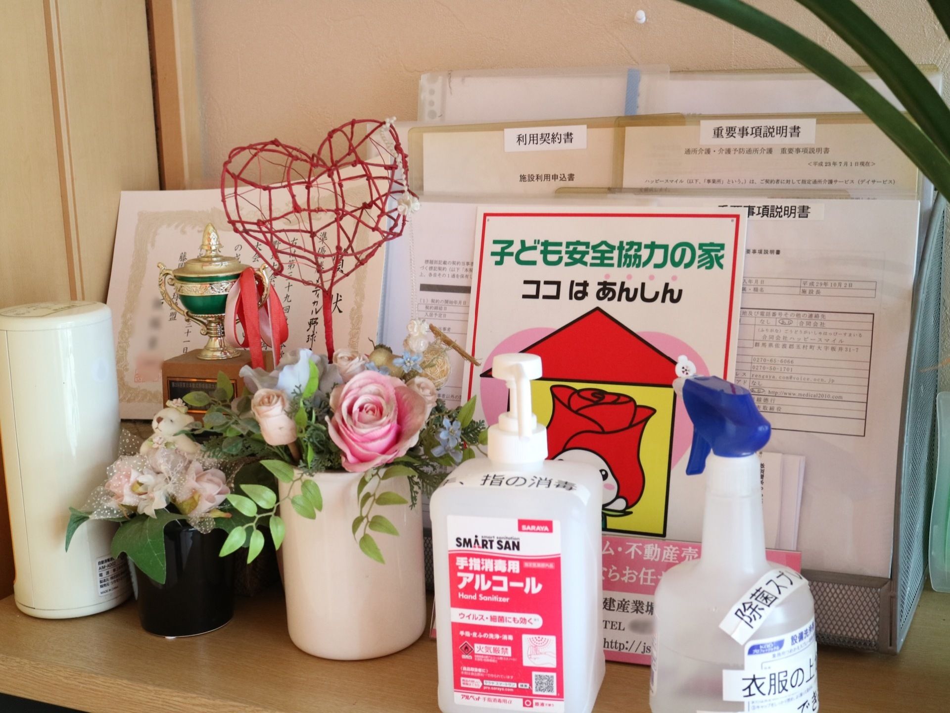 木製のカウンターの上に、トロフィーや賞状、除菌スプレー、花、さまざまな説明書や契約書が入れられたラックが置かれている。