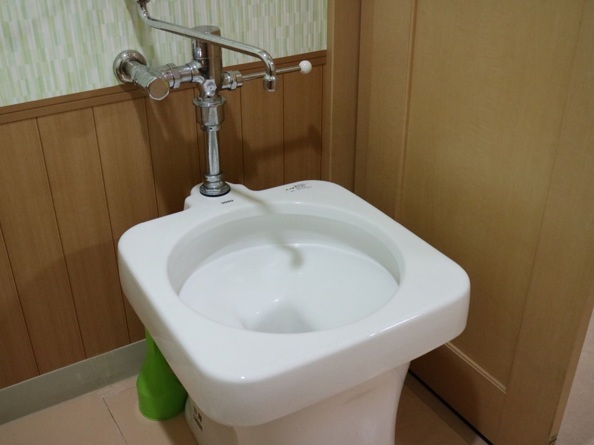 汚物流しがある。後ろの壁はデザイン性のある壁紙が貼られており、下部は木のぬくもりが感じられる造りとなっている。