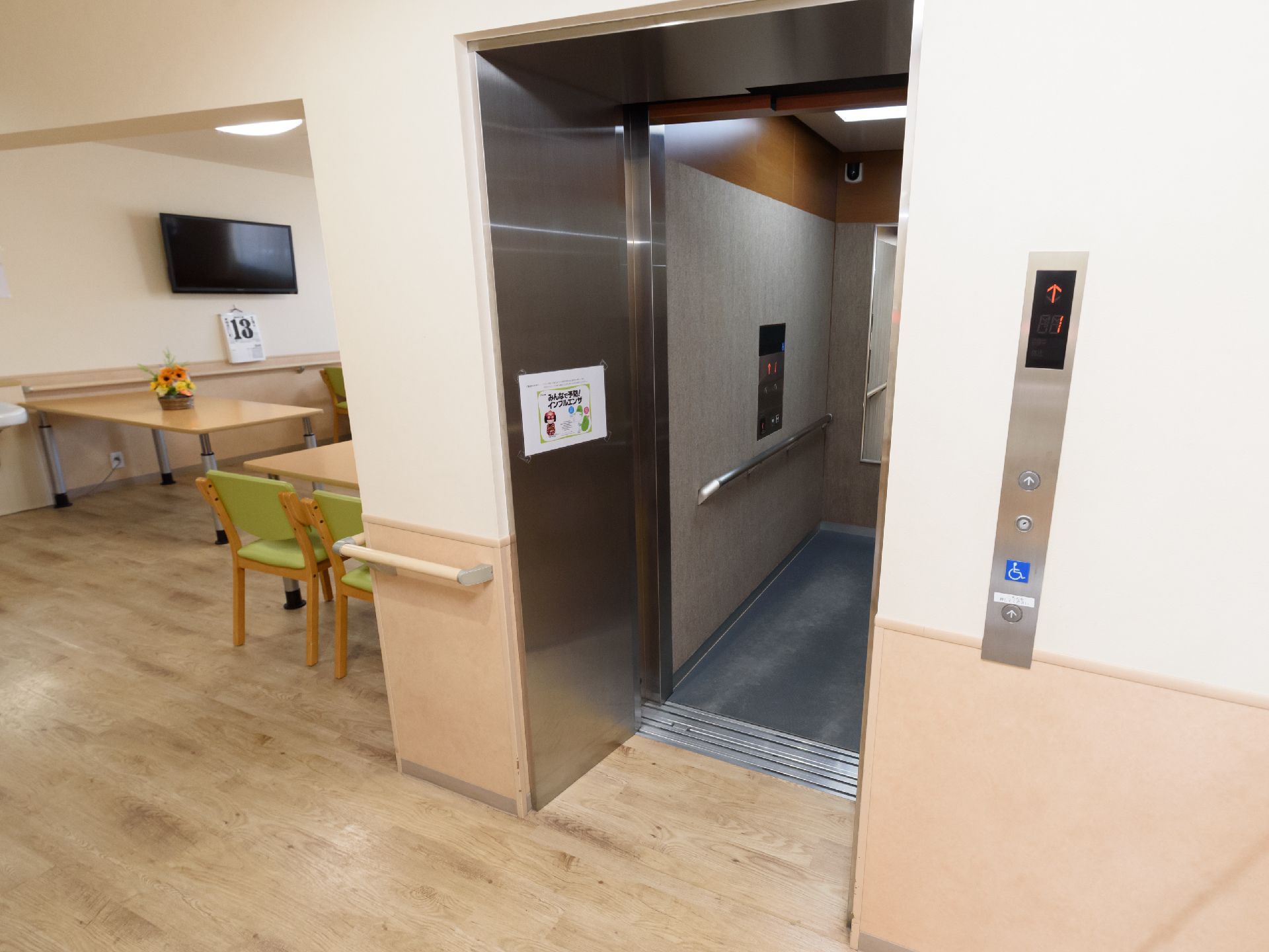 エレベーターが1階に止まっており、扉が開いている。奥行きがあり、左側の壁には手すりが設置されている。